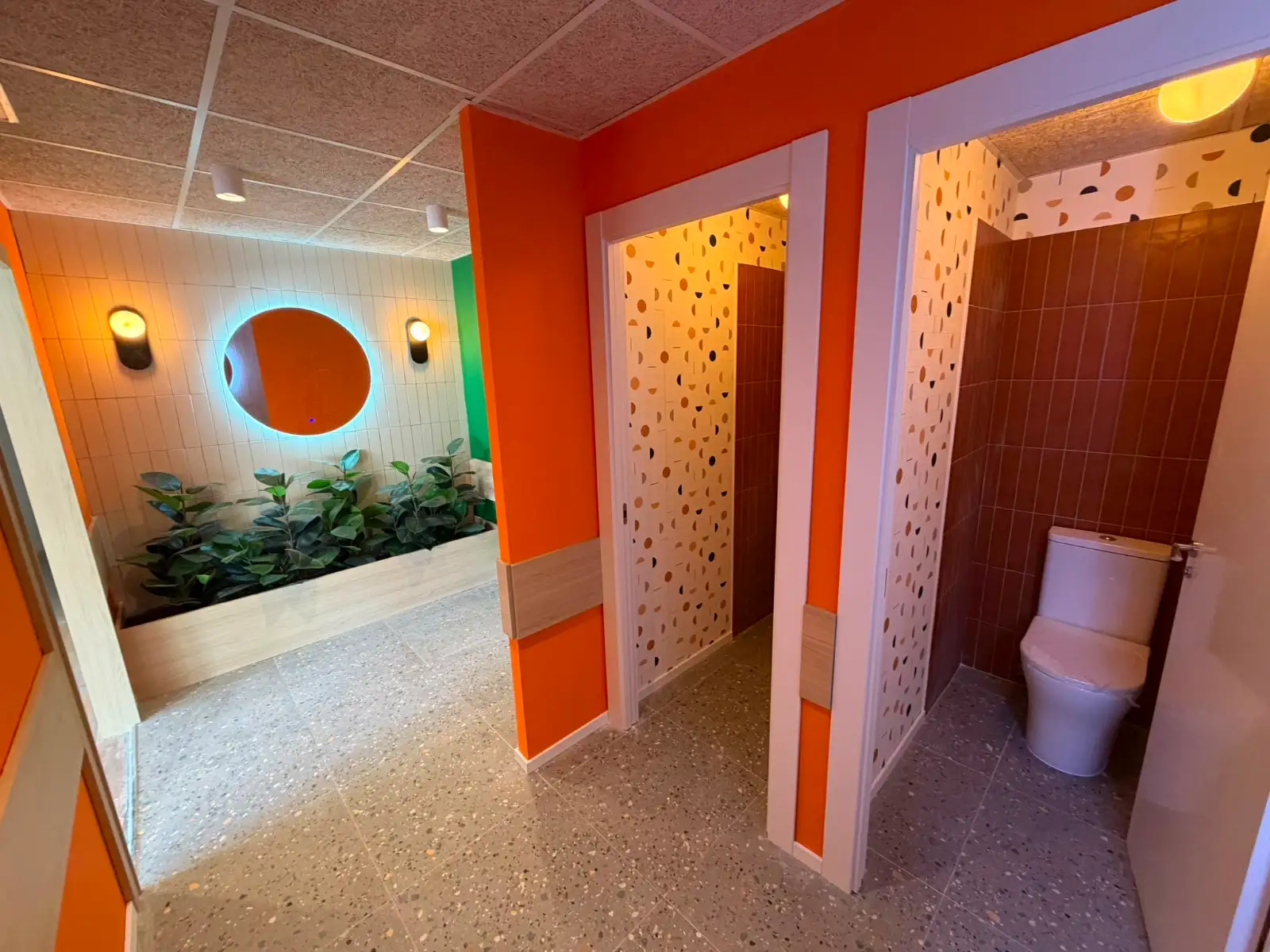 Reforma baño con diseño moderno de paredes naranjas, suelo de terrazo y jardín interior en Madrid