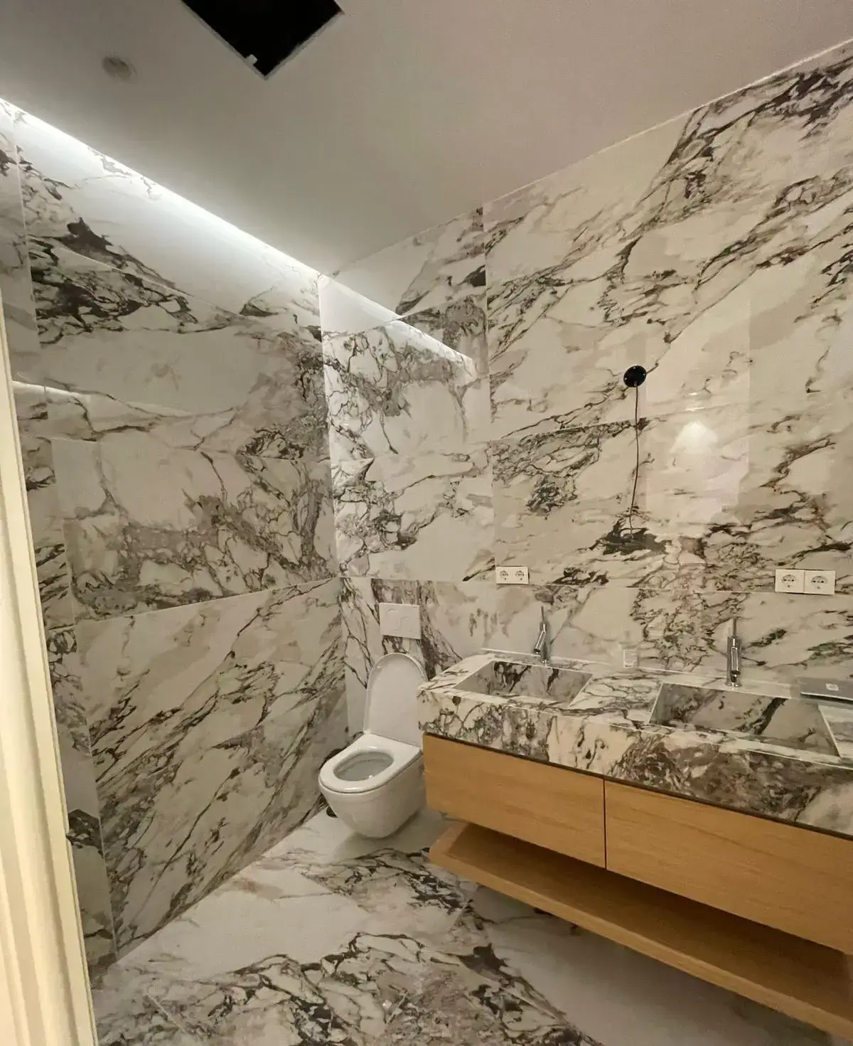 Reforma baño con revestimiento de mármol veteado y mueble de madera suspendido en Madrid